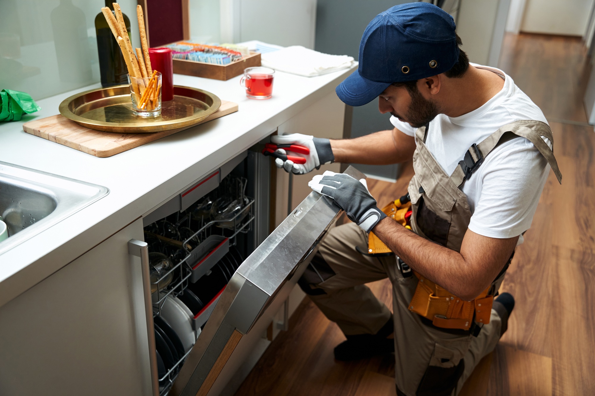 Young repairman or service worker repairing dishwasher appliance in kitchen while use special tools